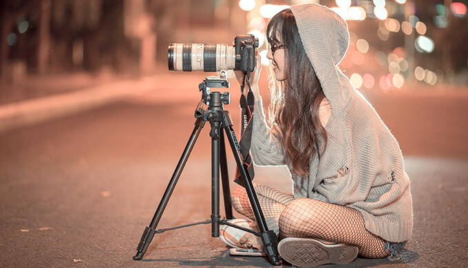 夜に道路の真ん中でフードを被った女性がカメラの前に座っている画像