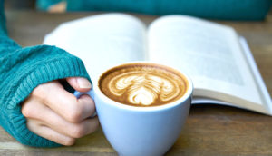 本を読みながらカフェラテを飲んでいる女性の手の画像