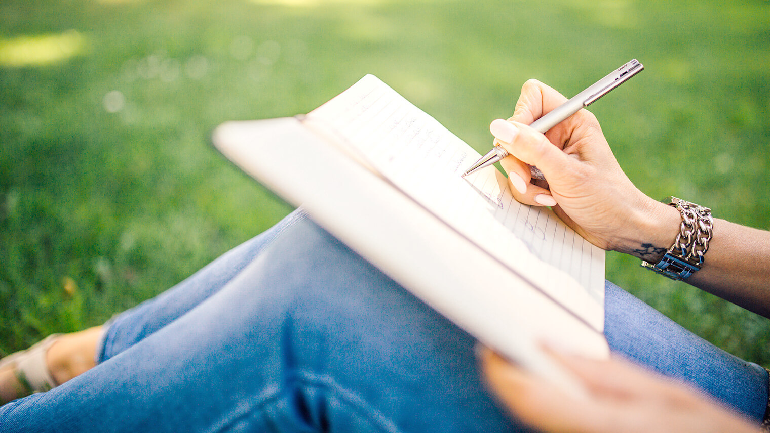 公園でノートを広げてペンで何か書いている女性の写真