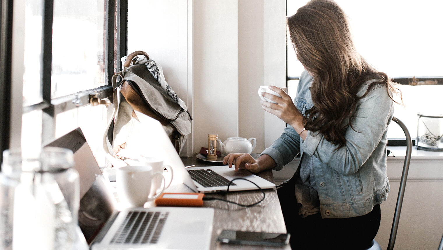 PCに向かってコーヒーを飲みながら作業している女性の画像