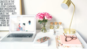 白い机の上に、macやお花、ノートやメガネが置かれている画像